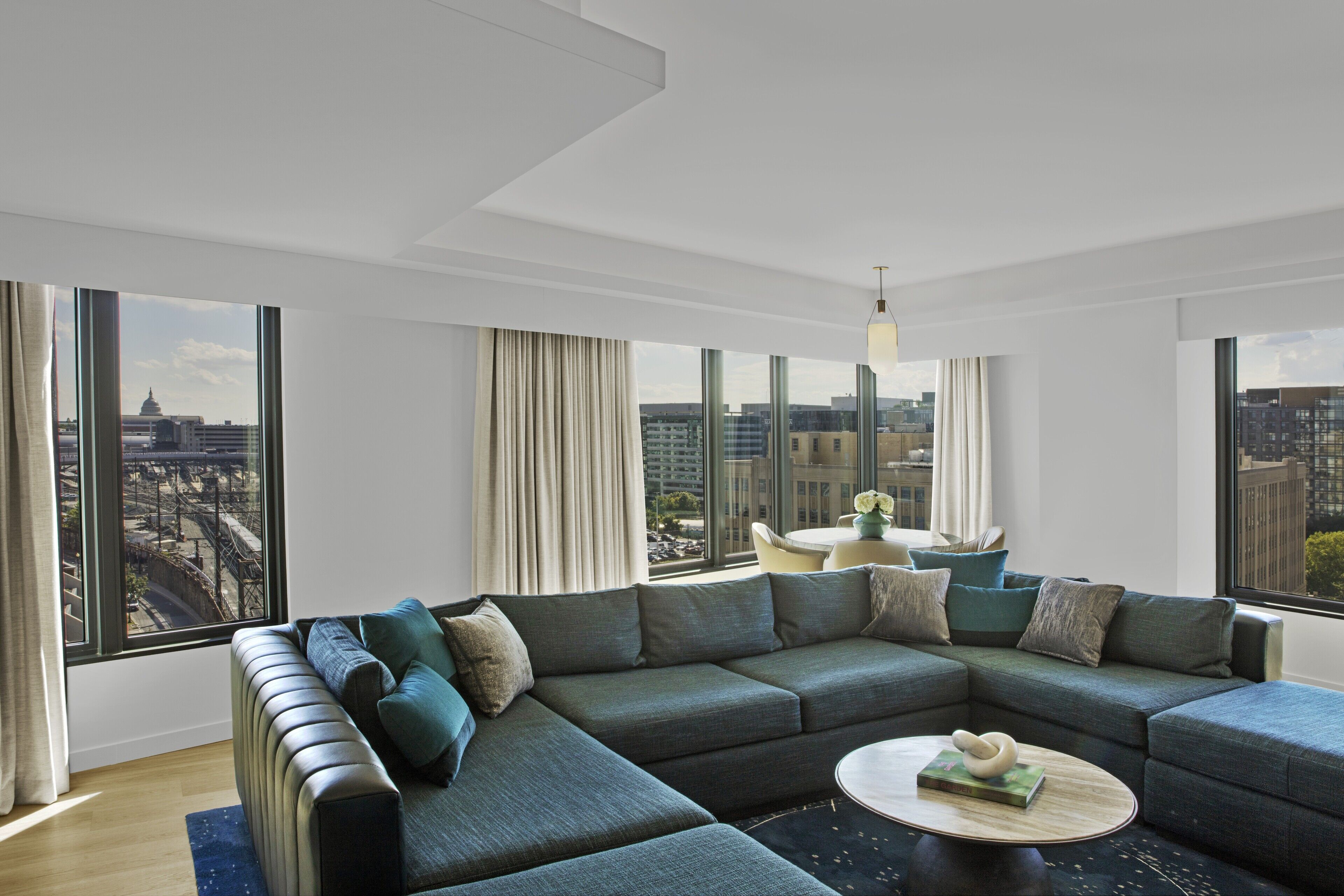 A modern living room with a sectional sofa, a round coffee table, and large windows offering a city view.