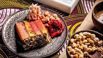 A dessert platter with various sweets and a bowl of chickpeas on a patterned tablecloth.