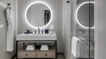 A modern bathroom with a round mirror, white tiles, a vanity with a sink, and a glass shower enclosure.