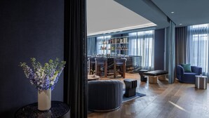 A modern bar area with a wooden floor, a seating area with a sofa and ottoman, and a bar counter with shelves of bottles.