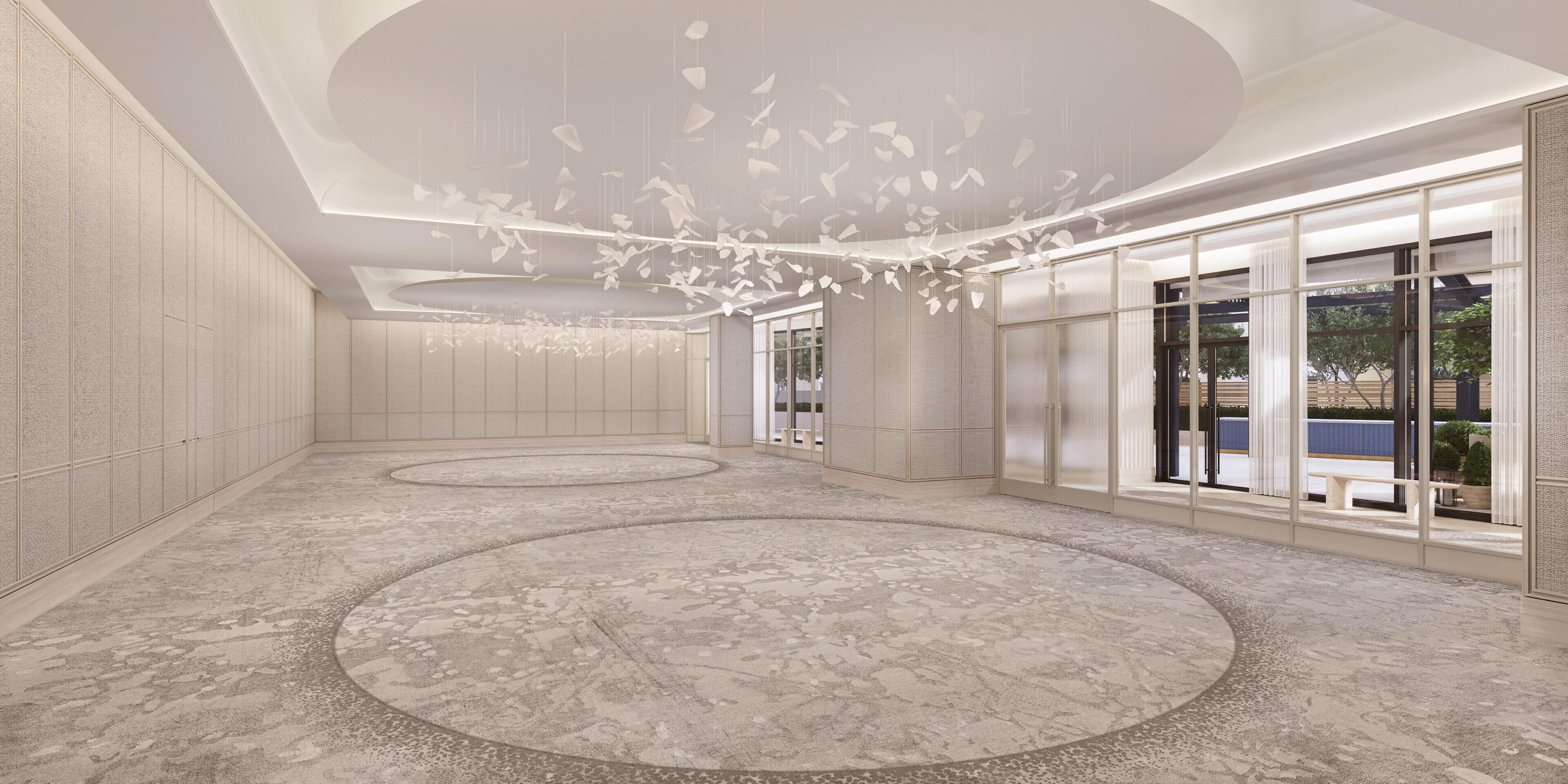 A spacious lobby with a circular floor pattern, a modern chandelier, and large windows offering views of the outdoors.