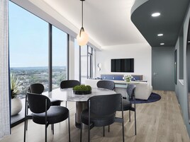 Un comedor moderno con una mesa redonda, seis sillas, una planta en maceta y vistas a la ciudad a través de grandes ventanales.