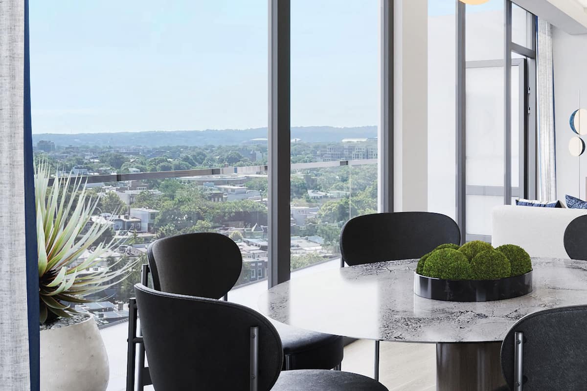 A modern dining area with a round table, black chairs, and a view of a cityscape through large windows.