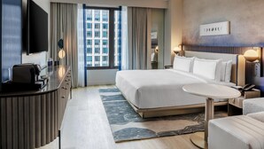 A hotel room with a bed, bedside table, TV, and a view of the cityscape.