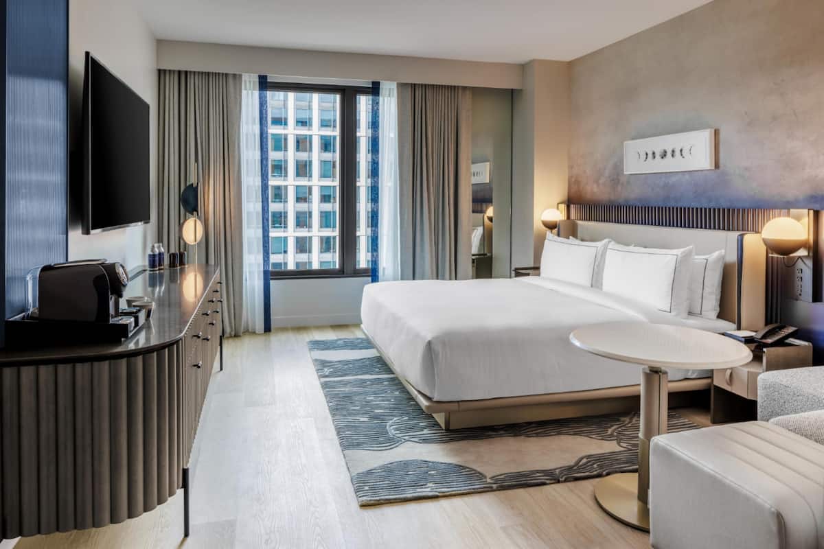 A hotel room with a bed, bedside table, TV, and a view of the cityscape.