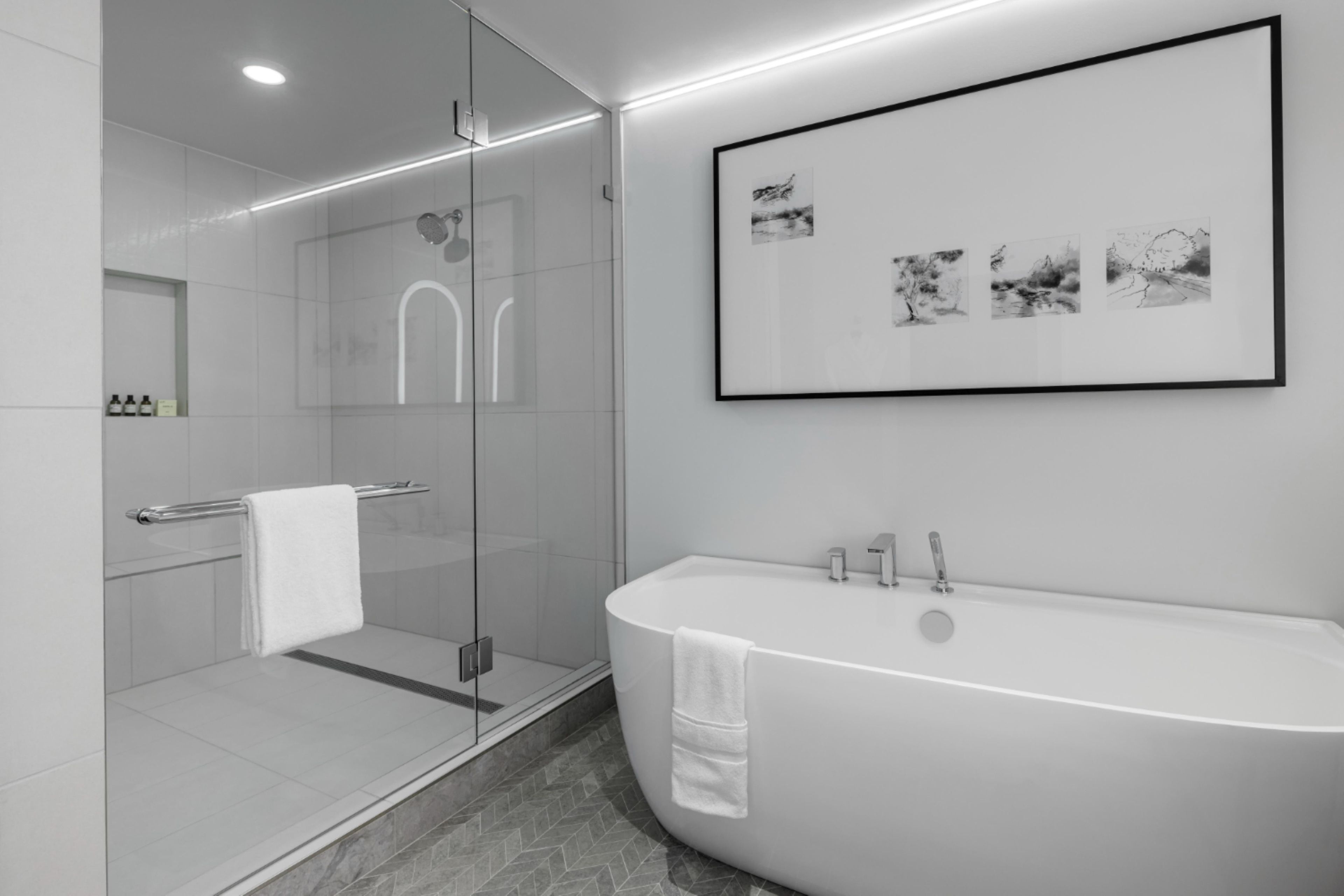 Une salle de bain moderne avec une douche à parois de verre, une baignoire sur pieds et une œuvre d’art encadrée au mur.