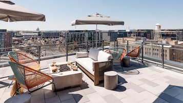 A rooftop terrace with outdoor seating, a table with drinks, and a city view.