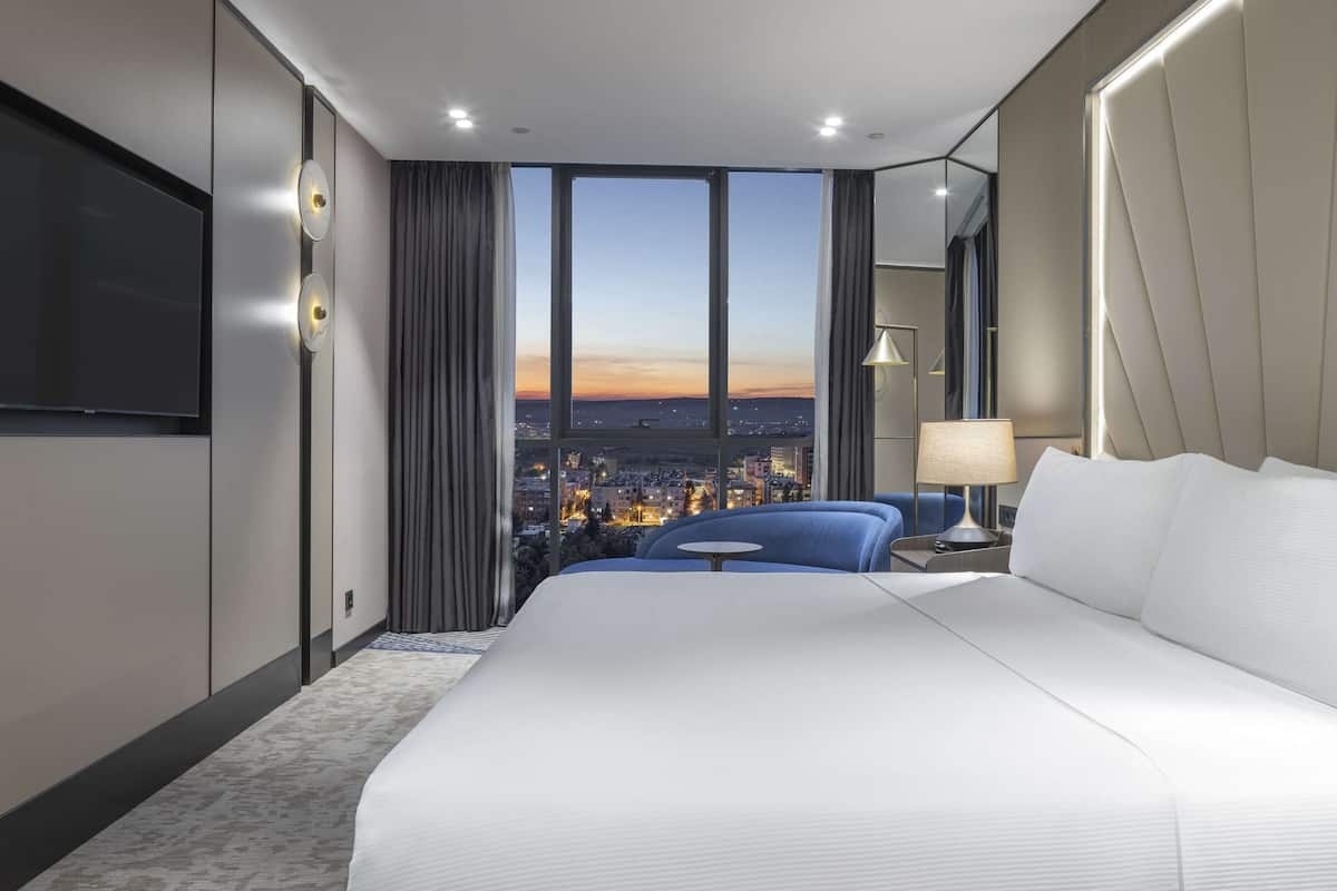 A hotel room with a large bed, a TV, a city view, and a modern design.