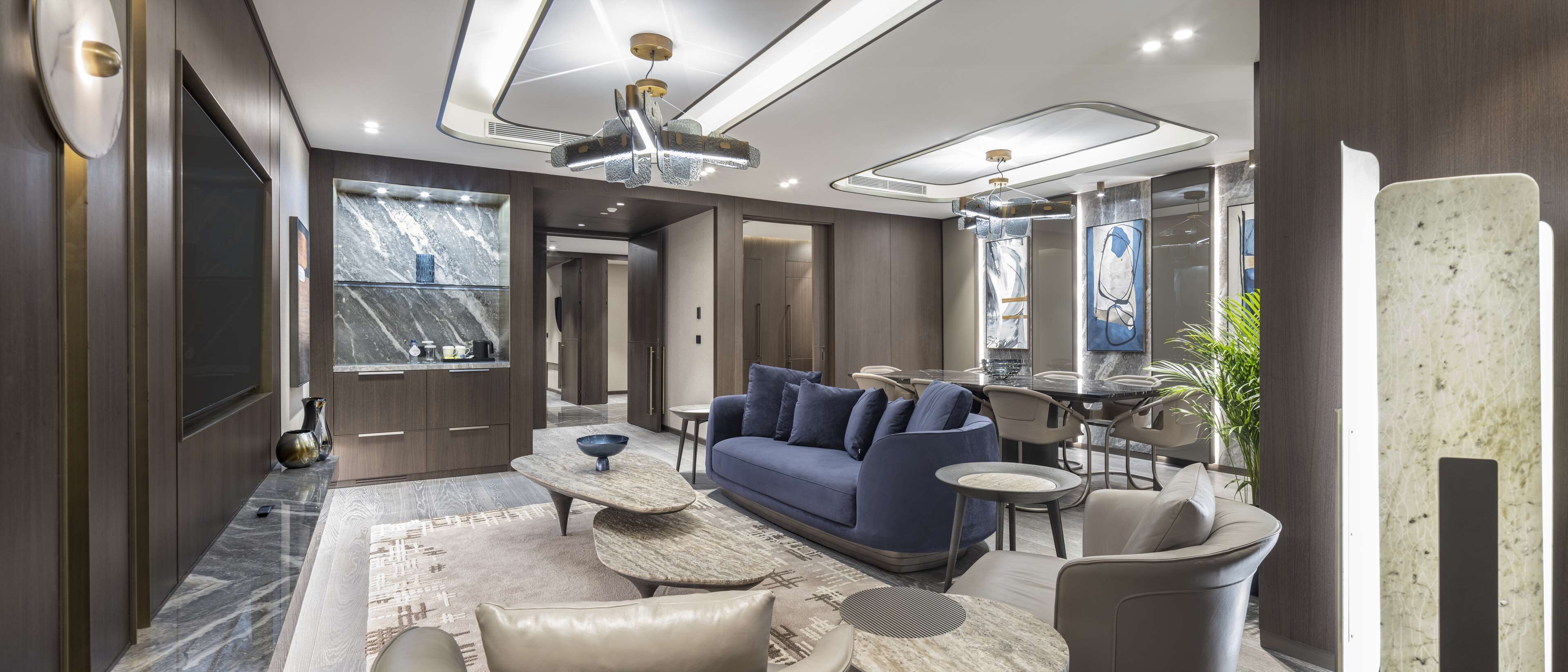 A modern living room with a blue sofa, a coffee table, and a dining area with a round table and chairs.
