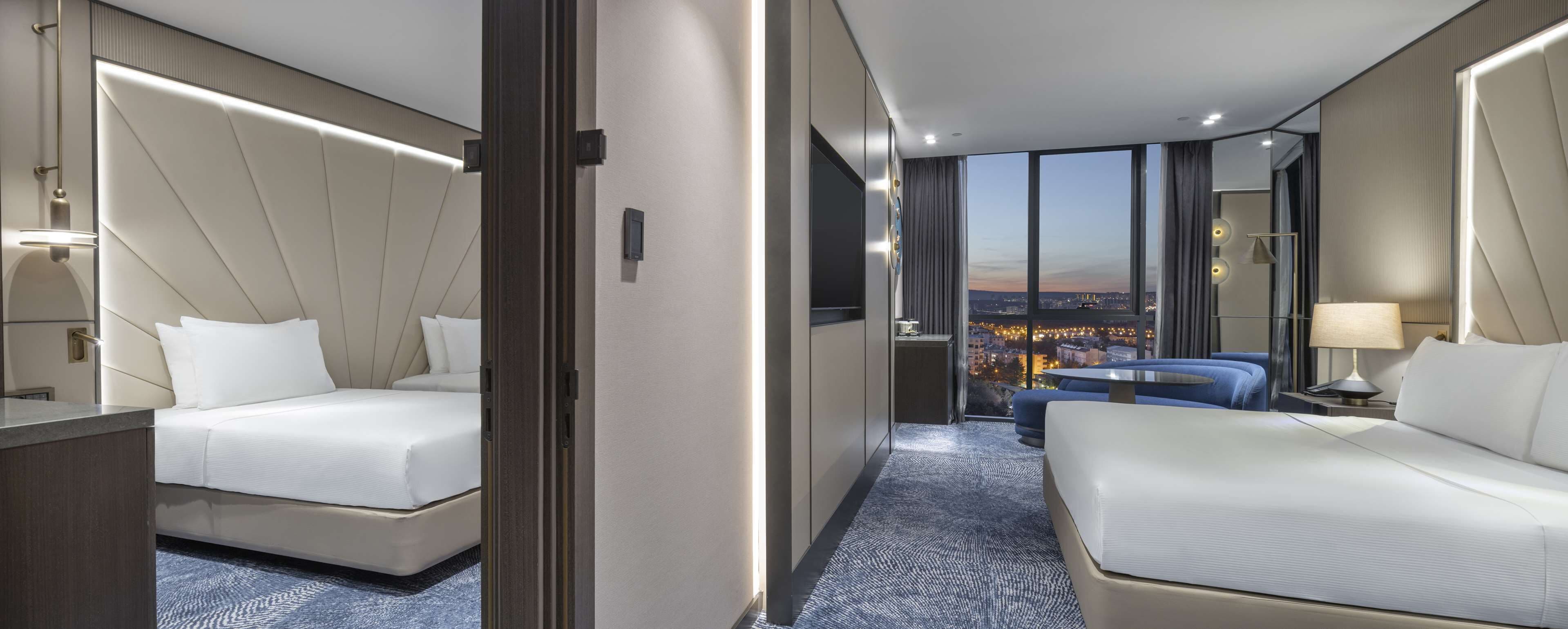 A hotel room with two beds, a view of the cityscape, and a modern design.