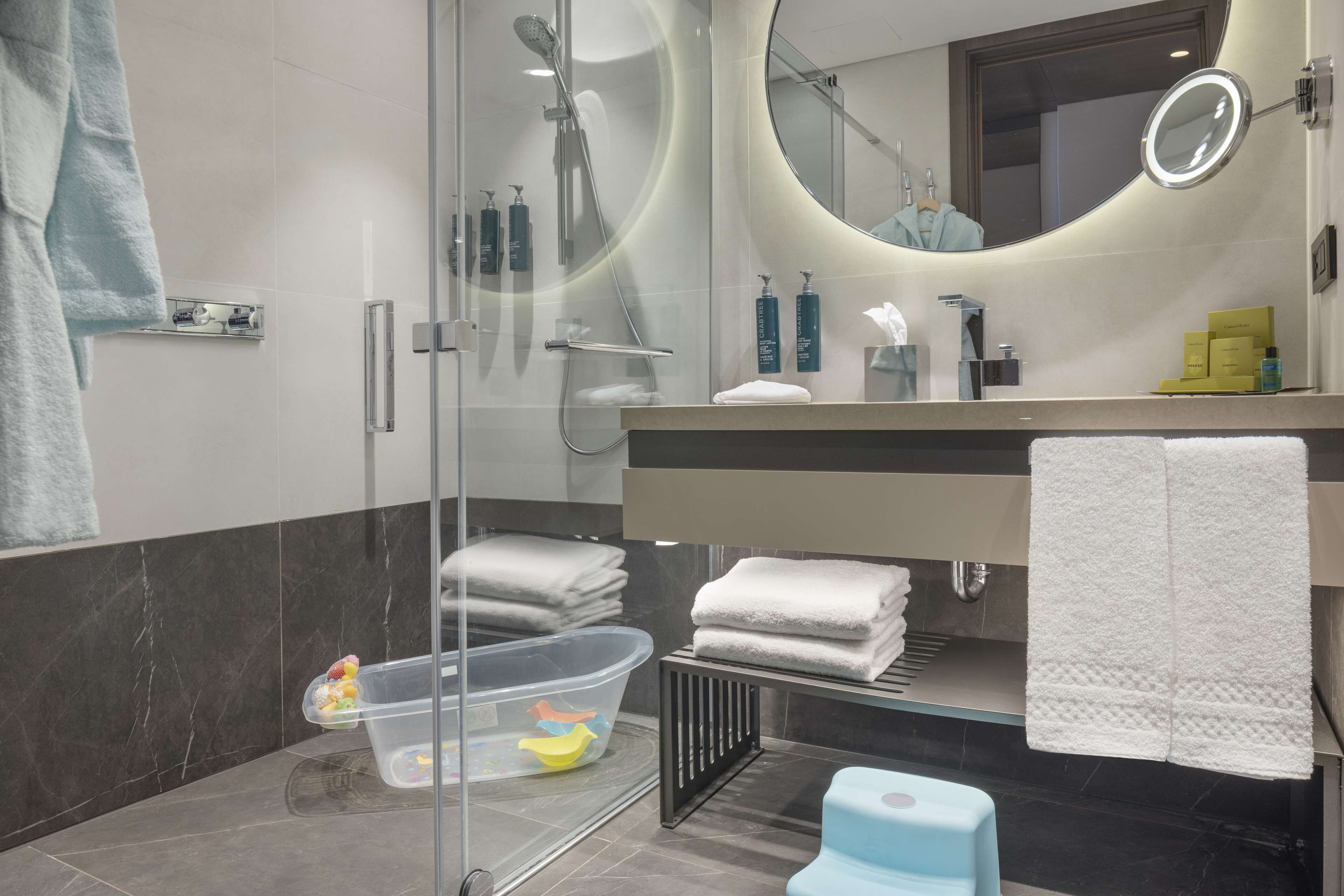 A modern bathroom with a glass shower enclosure, a round mirror, and neatly folded towels.