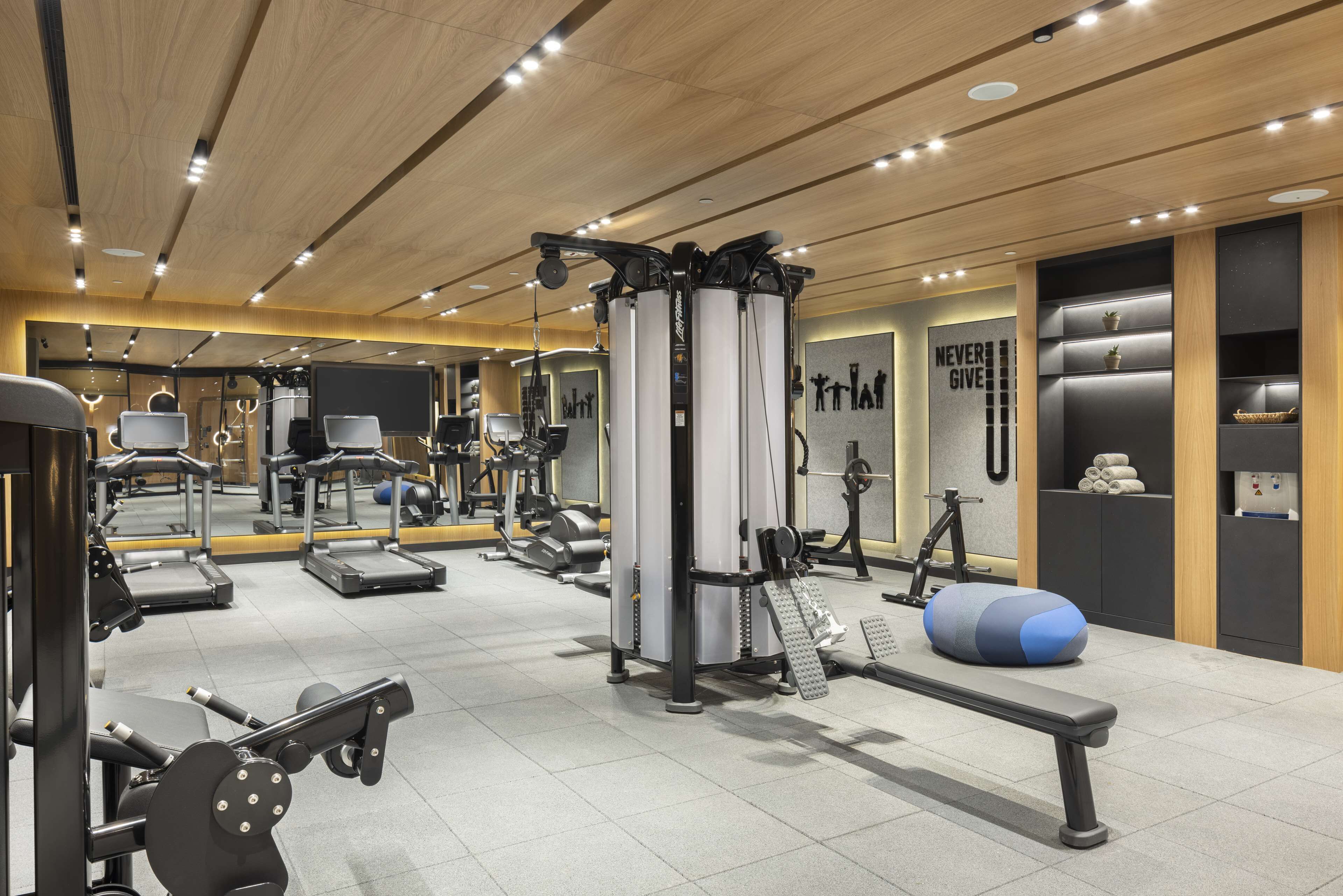 Un gimnasio moderno con diversos equipos de ejercicio, una banca y una pared motivacional.