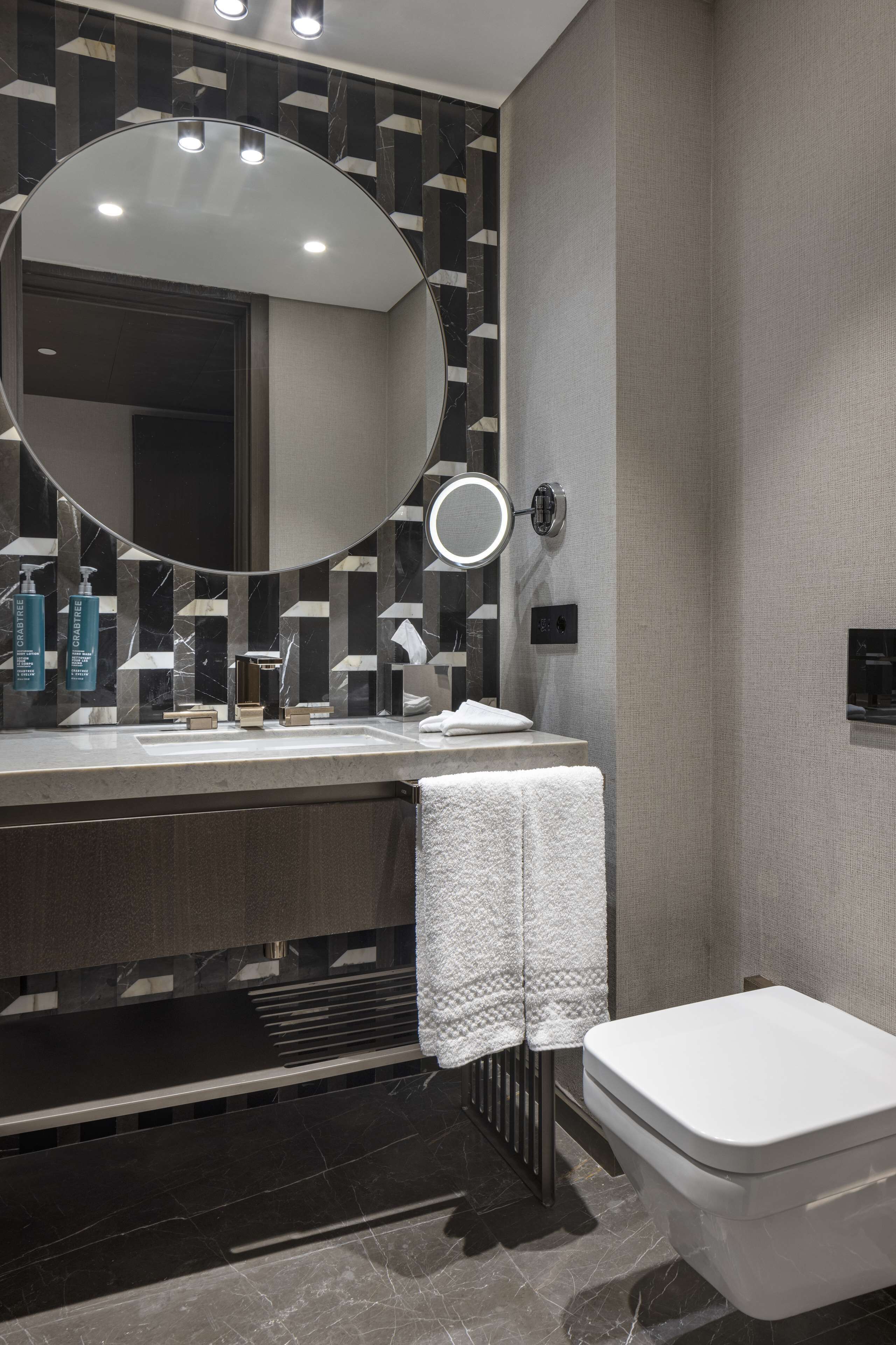 Een moderne badkamer met een ronde spiegel, een toilet en een wastafel met toiletartikelen.