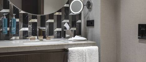 A modern bathroom with a round mirror, a toilet, and a vanity with toiletries.
