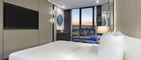 A modern hotel room with a large bed, a TV, a city view, and a small table.