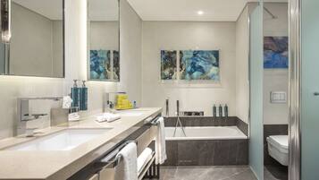 A modern bathroom with two sinks, a bathtub, and a toilet. There are towels and toiletries on the counter.
