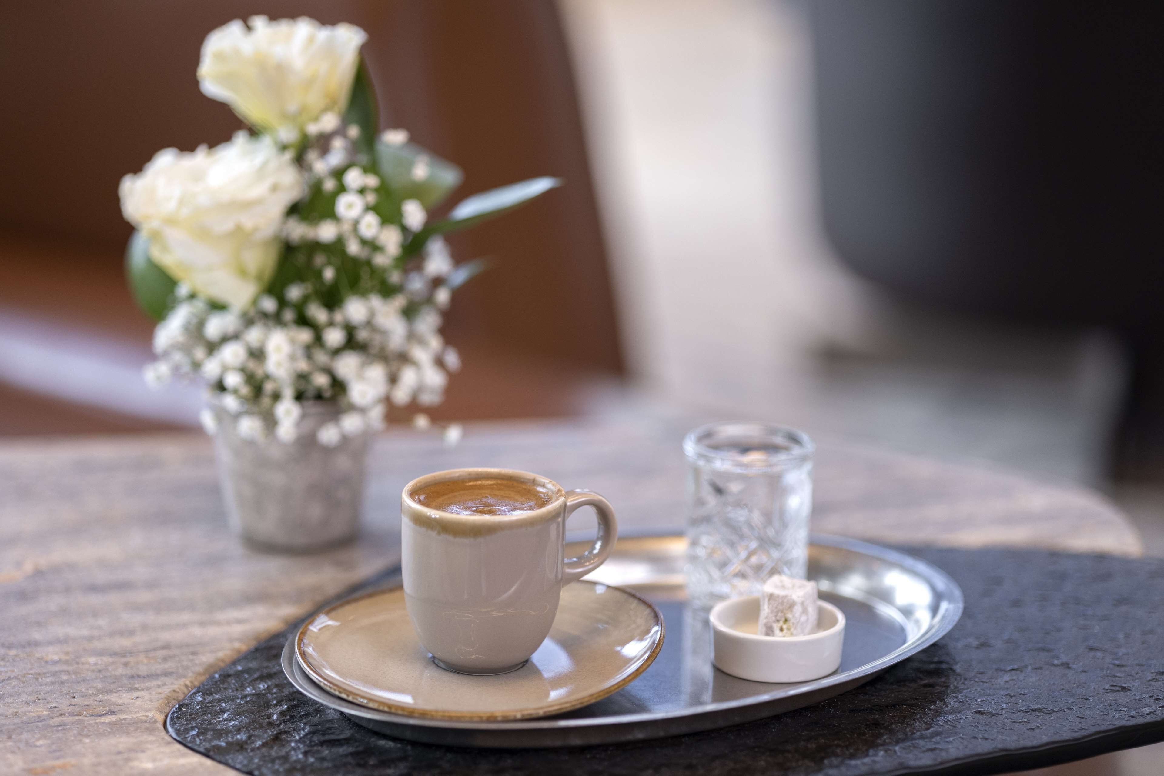 Una taza de café sobre una bandeja con un pequeño jarrón de flores y un azucarero.