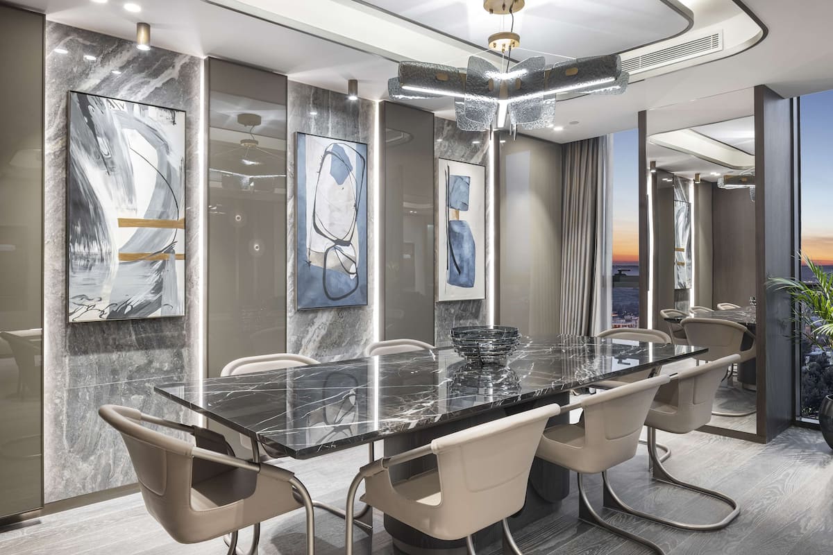 A modern dining area with a marble table, beige chairs, and abstract art on the walls.