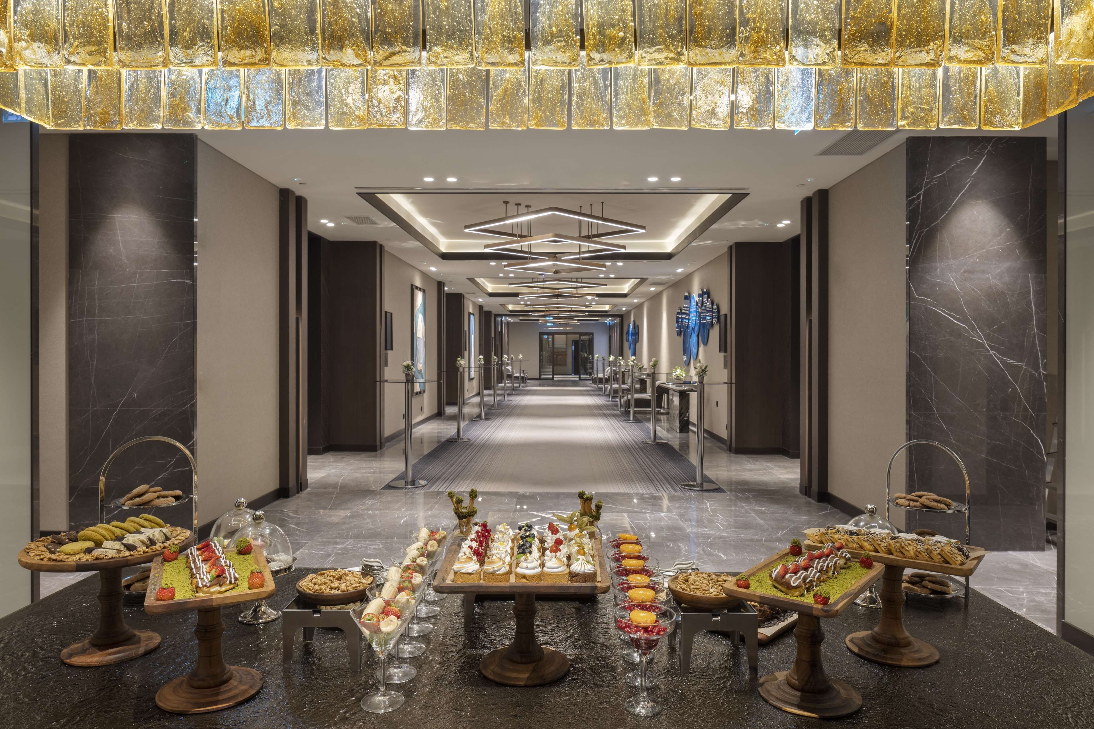 A hotel corridor with a long reception area, multiple display cases with food, and a modern ceiling design.