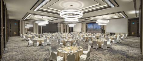 A large banquet hall with round tables, white chairs, and chandeliers.