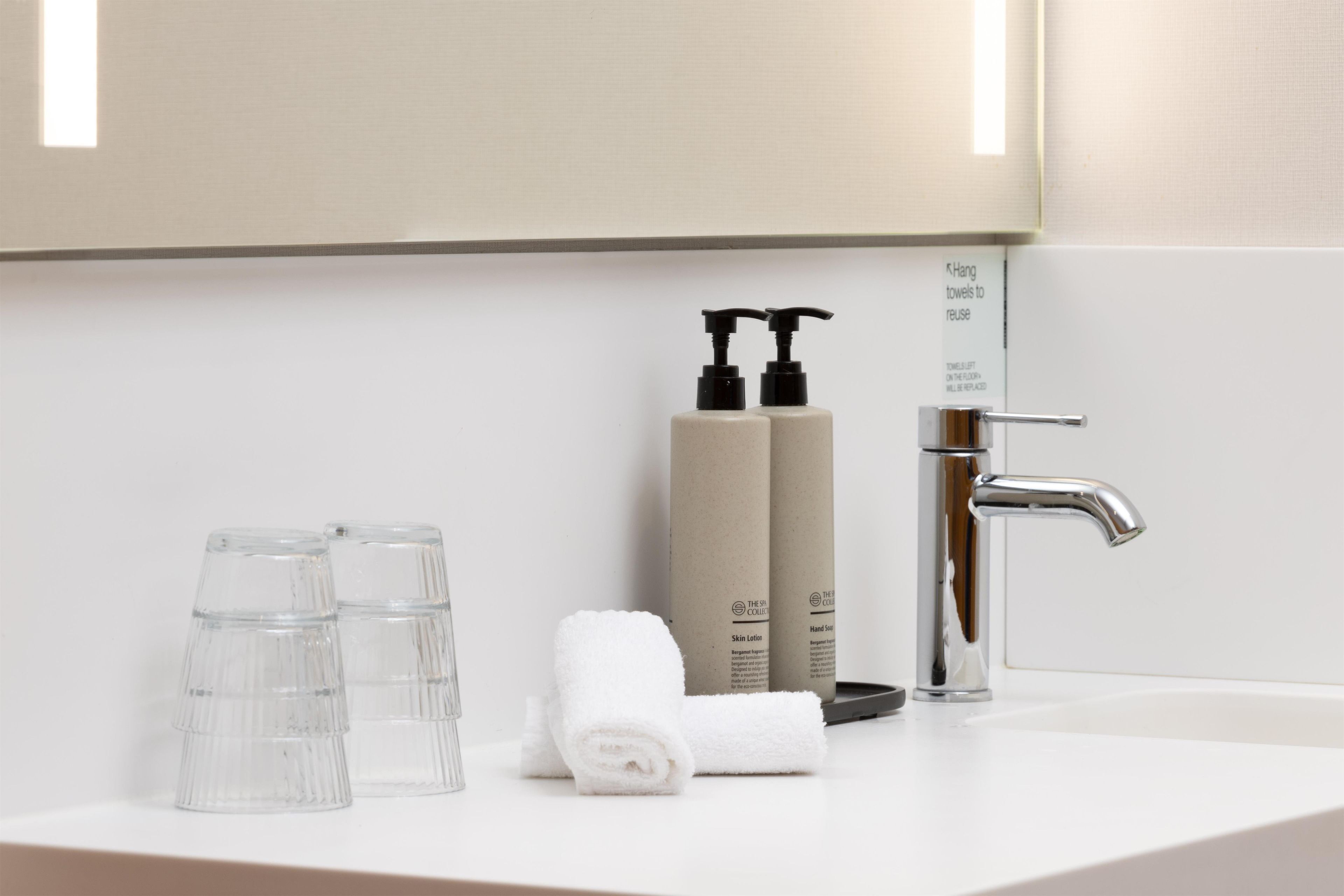 A bathroom sink with a mirror above it, a towel, two bottles of hand soap, and two glass bottles.