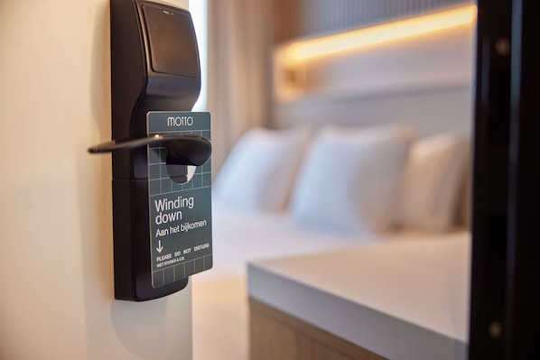 A hotel room with a bed, a bedside table, and a wall-mounted device with a sign that reads "Winding down" and "Please do not disturb."
