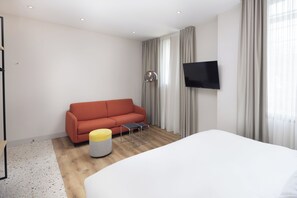 A modern hotel room with a large bed, a red sofa, a small table, and a TV mounted on the wall. - Motto by Hilton Rotterdam City Centre (Rotterdam)