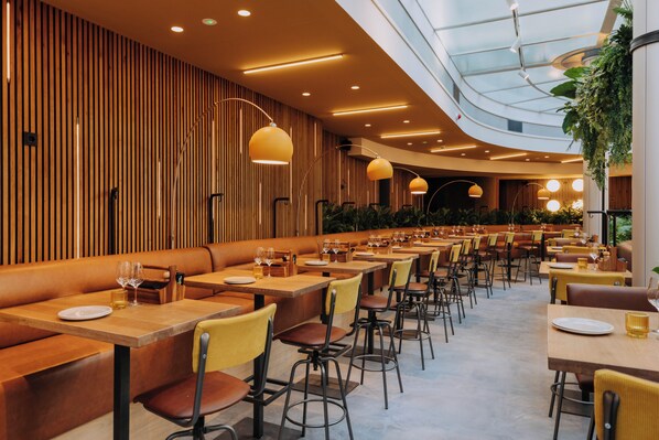 Un restaurante moderno con paneles de madera, mesas largas y sillas amarillas.