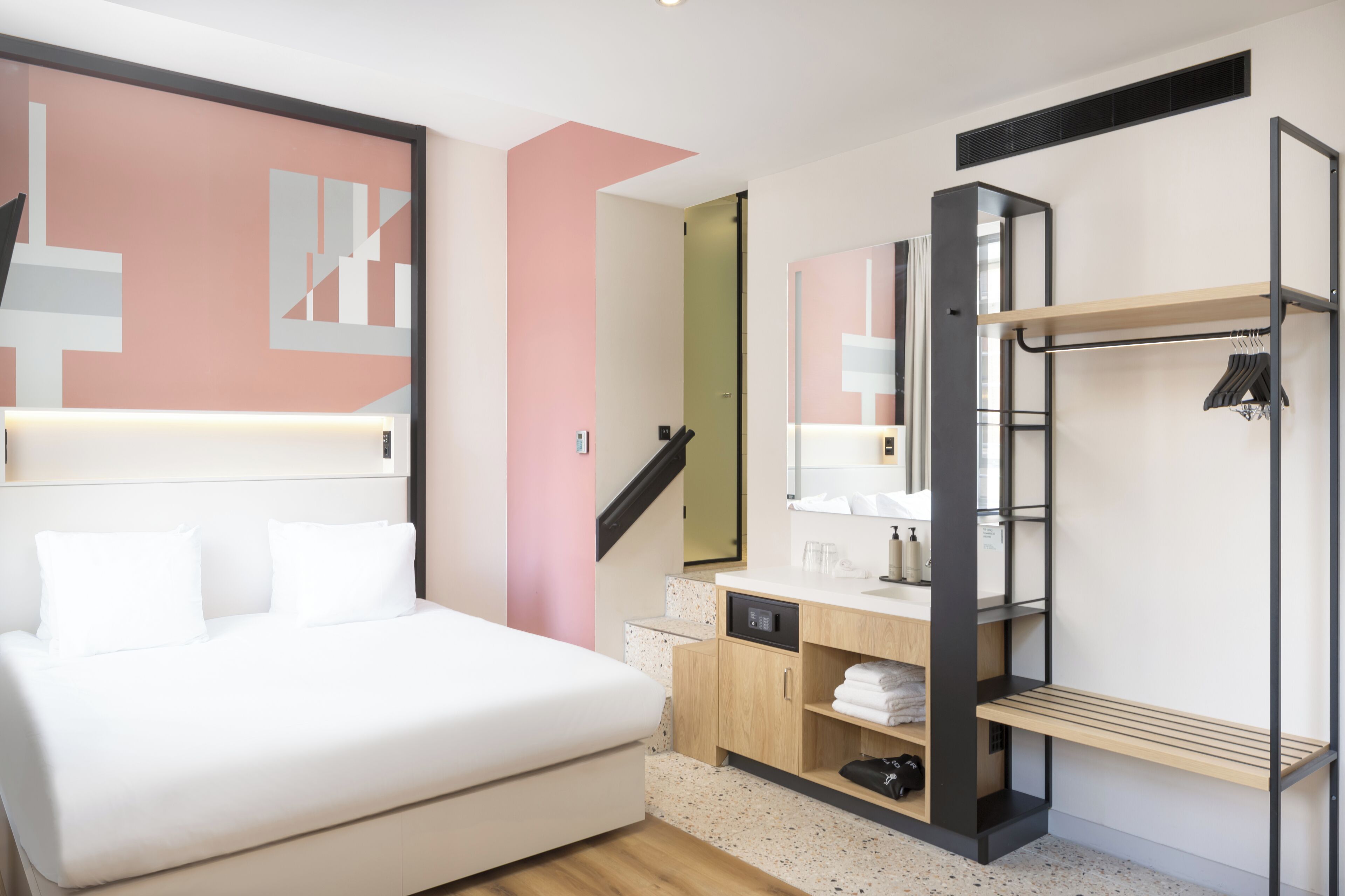 A modern bedroom with a bed, a vanity with a mirror, a built-in wardrobe, and a staircase.