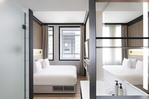 Habitación de hotel con una cama grande, una mesita de noche con artículos de aseo, un espejo y una ventana con cortinas.