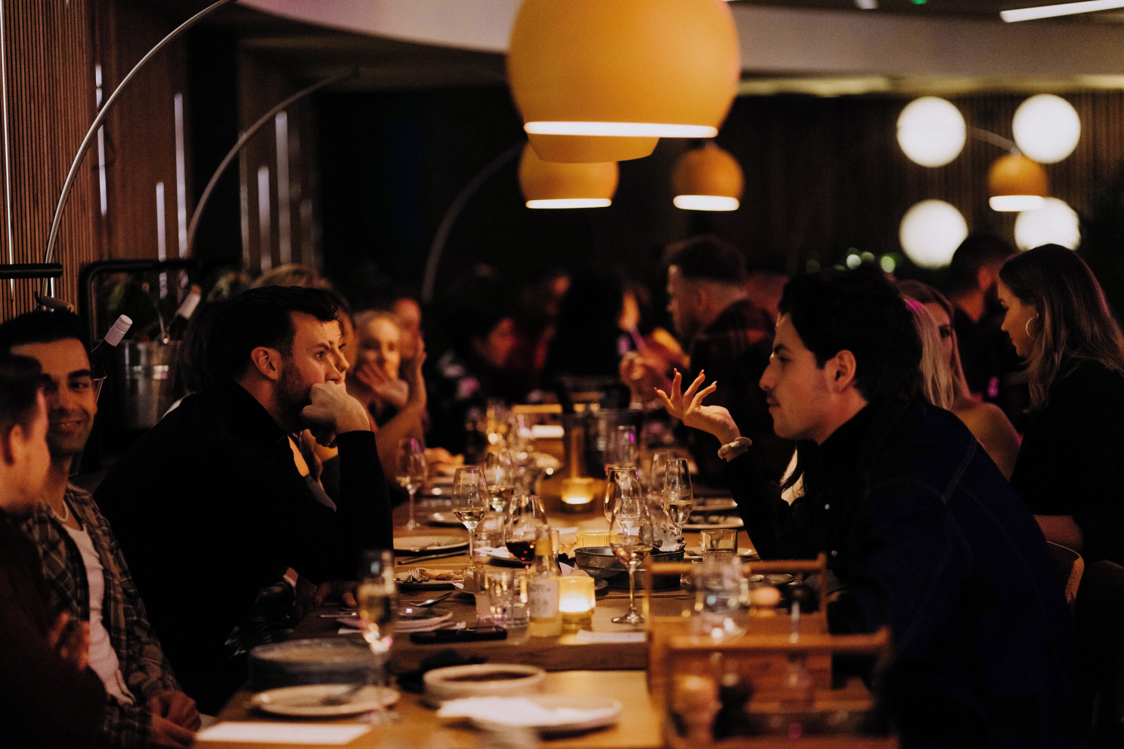 Un restaurante con una larga mesa dispuesta para un grupo de personas, varios platos y vasos sobre la mesa, e iluminación colgante.