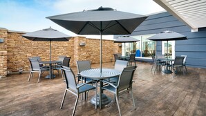 Ein Terrassenbereich im Freien mit runden Tischen und Stühlen, großen Sonnenschirmen und einer Steinmauer.