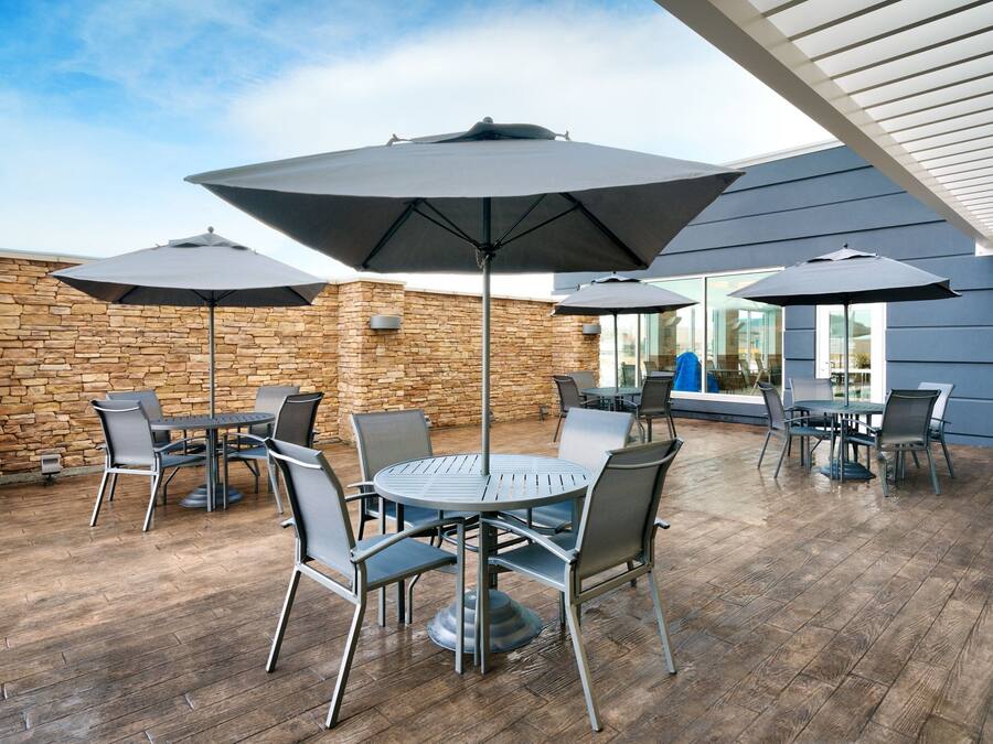 Un espace extérieur aménagé en terrasse, avec des tables et des chaises rondes, de grands parasols et un mur en pierre.
