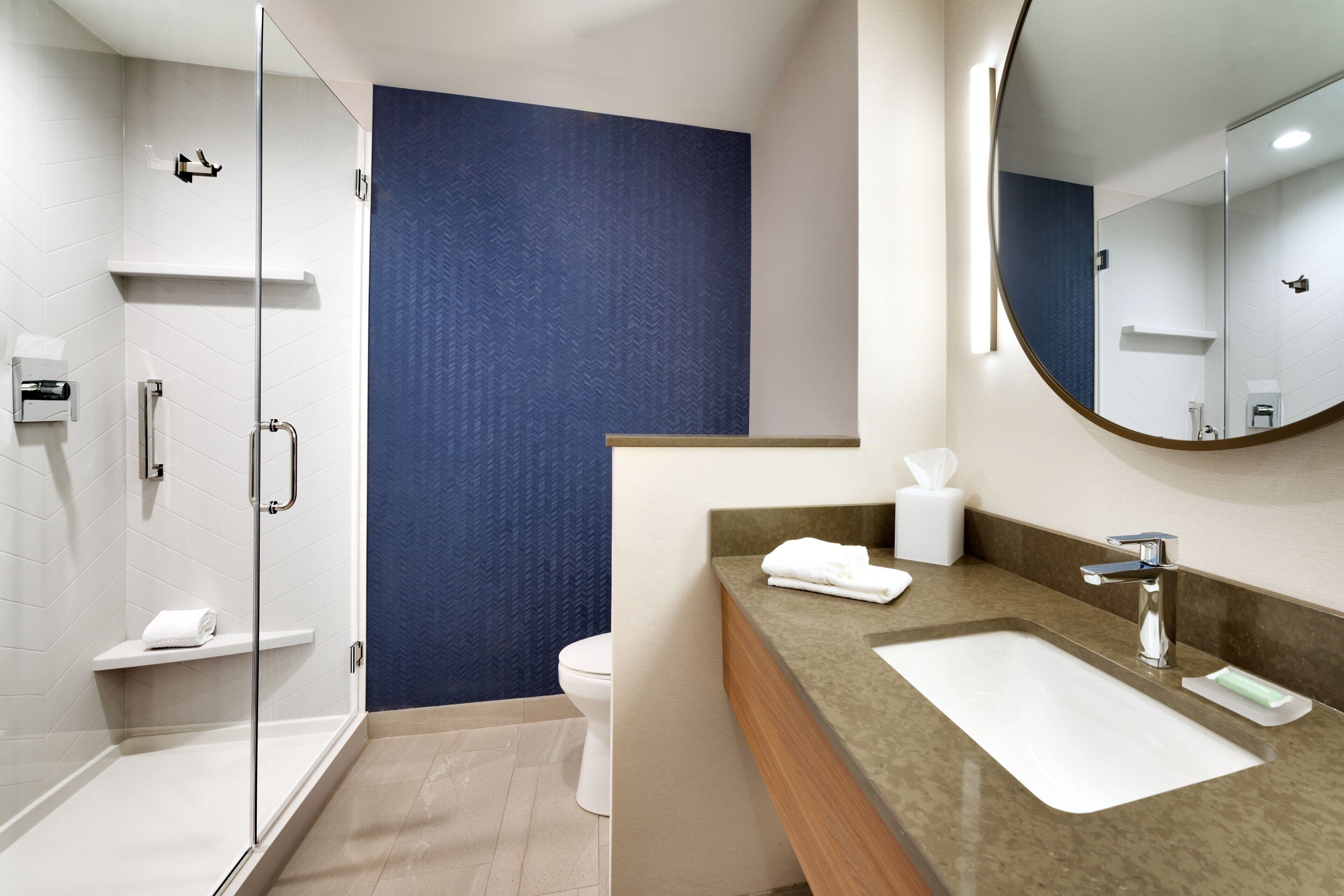 A modern bathroom with a glass shower enclosure, a white sink with a marble countertop, and a large mirror.