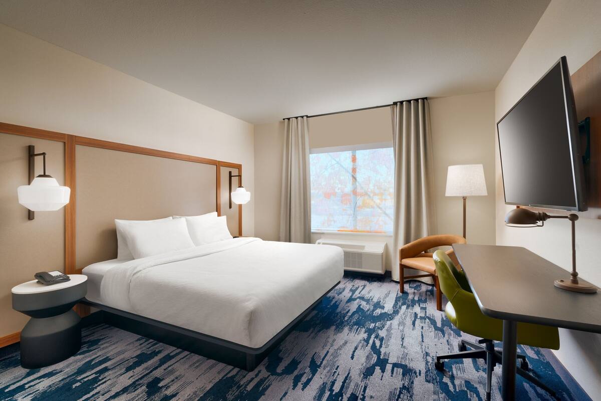 A hotel room with a large bed, a desk, a chair, a television, and a window with curtains.