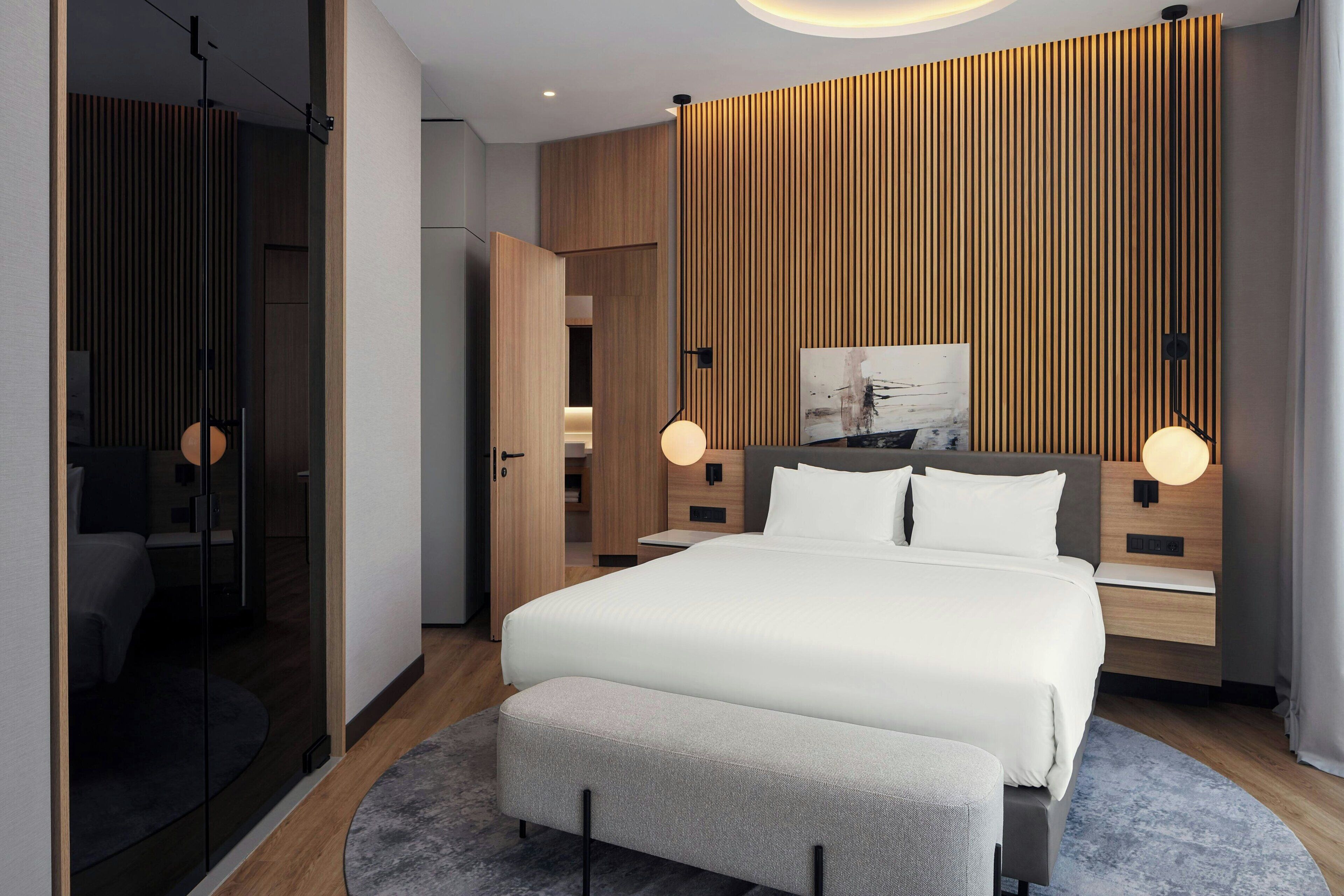A modern hotel room with a large bed, bedside tables, a wall-mounted artwork, and a wooden panel wall.