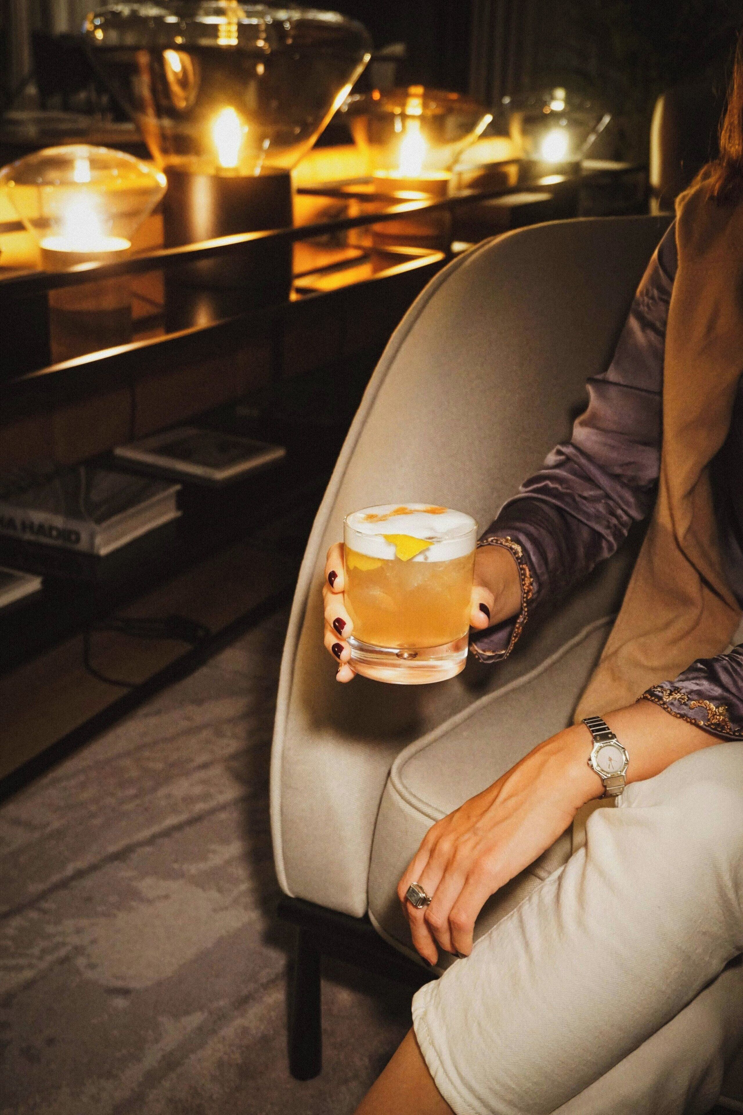 A person sitting on a chair holding a glass of drink, with a watch on their wrist.