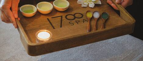 A wooden tray with bowls of bath salts and a candle, held by a person.