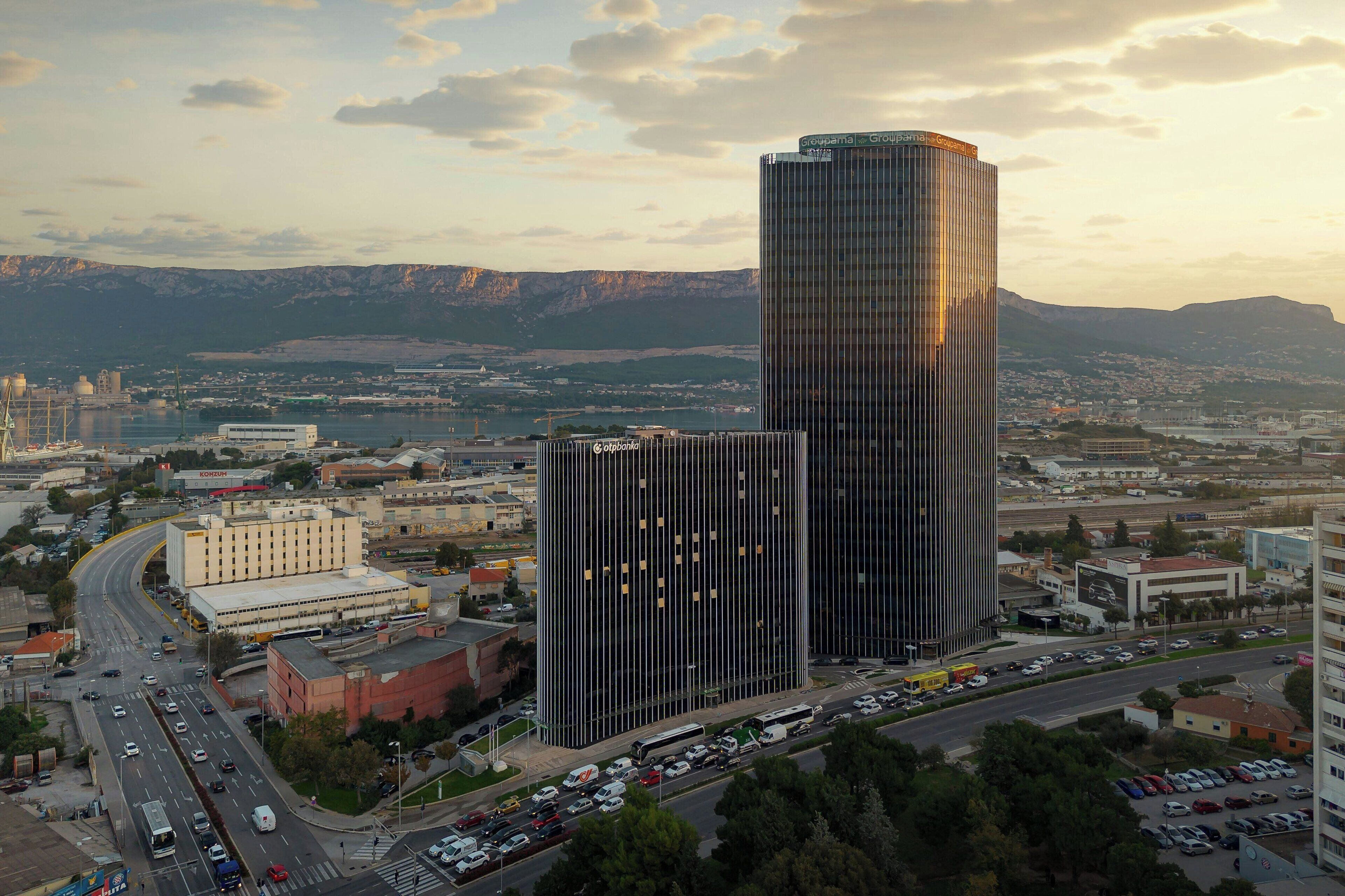 Un edificio de gran altura con fachada de vidrio moderna, rodeado por una zona urbana concurrida, con calles y otros edificios.