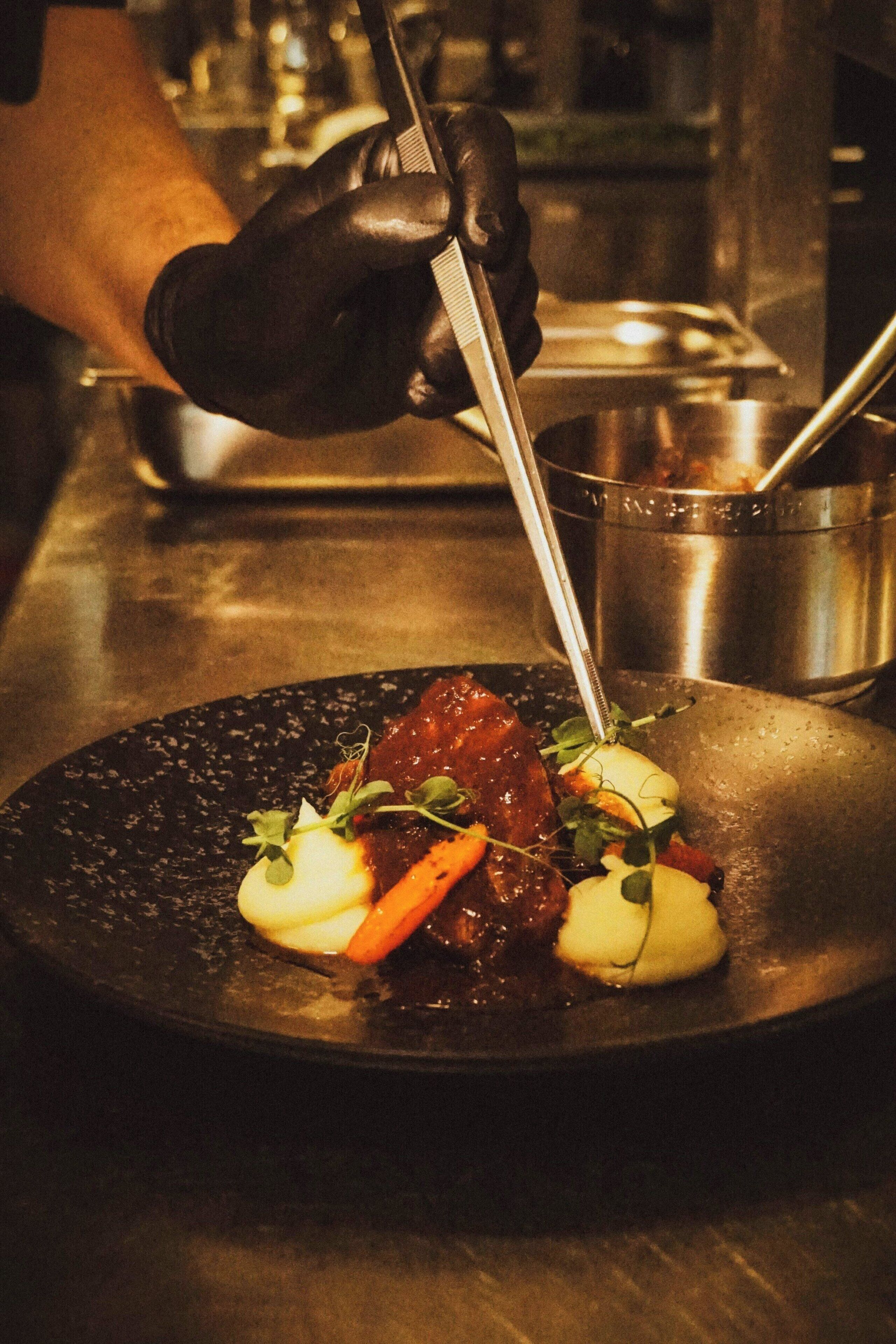 A chef preparing a dish with a pan, a pot, and a spoon.