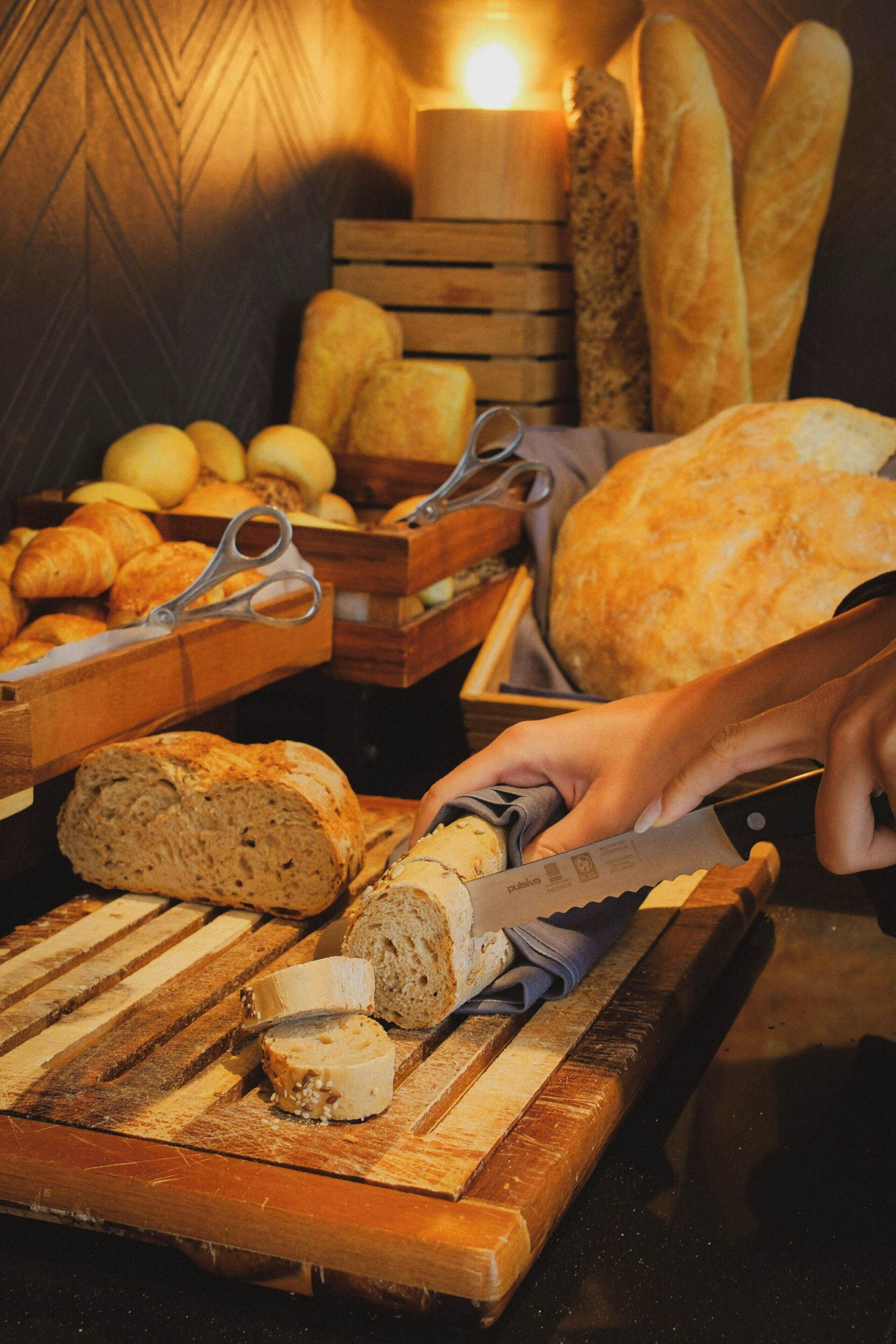 A wooden cutting board with sliced bread, a knife, and a pair of scissors on a table.