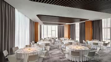 Un salón de conferencias amplio con mesas redondas, sillas blancas y un diseño moderno de techo.