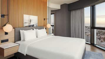 Habitación de hotel moderna con una cama grande, un panel de pared de madera, vista a la ciudad y una mesita de noche con una lámpara.