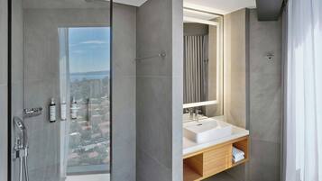 A modern bathroom with a large window, a shower, a sink, and a mirror.