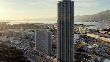 Un edificio alto con un design moderno, immerso in un paesaggio urbano con strade e altri edifici.