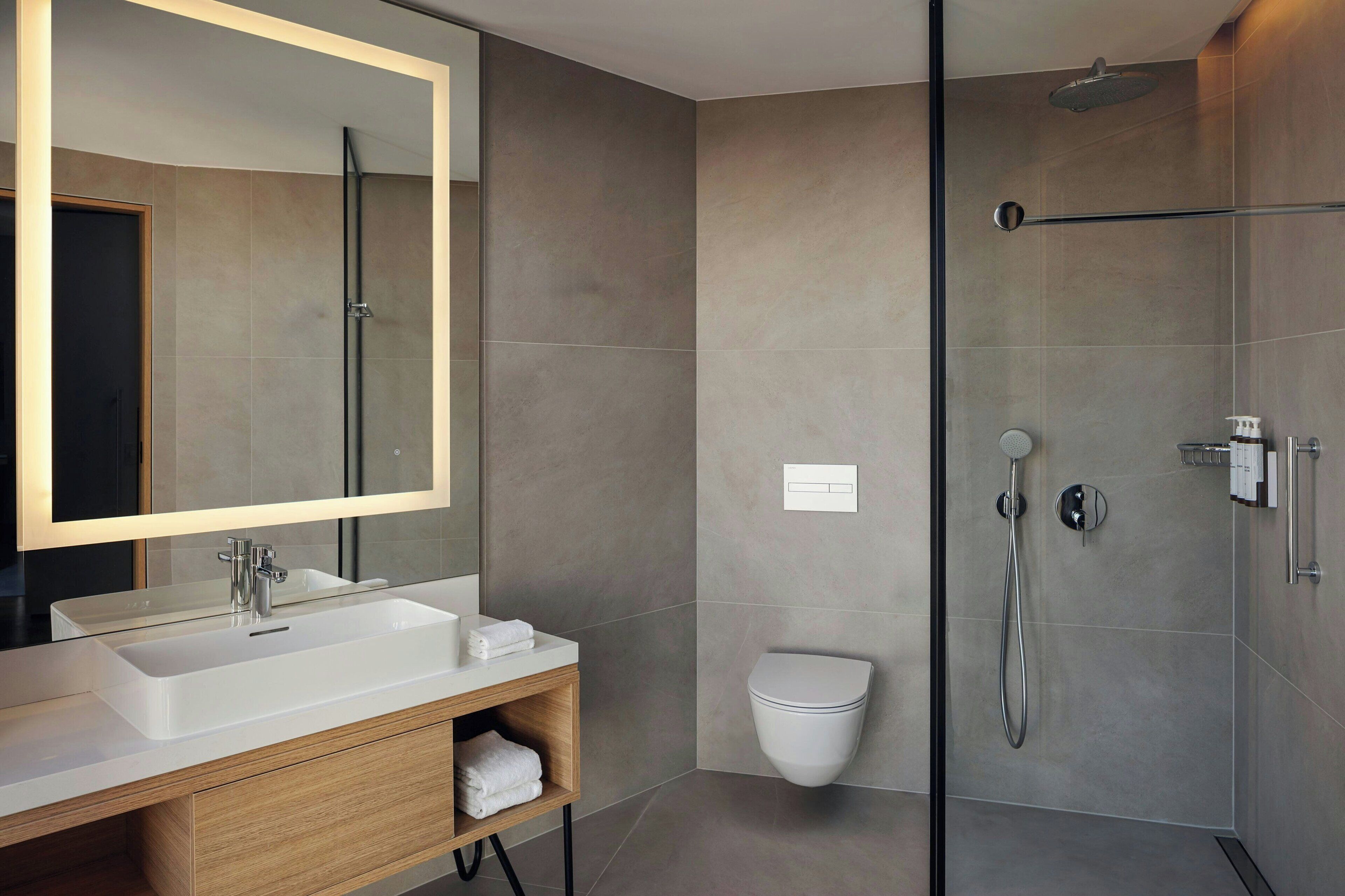 A modern bathroom with a large mirror, a white sink, a glass-enclosed shower, and a toilet.