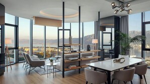 A modern hotel room with a large window offering a city view, a dining area with a table and chairs, and a cozy seating area with sofas and a bookshelf. - AC Hotel by Marriott Split (Split)