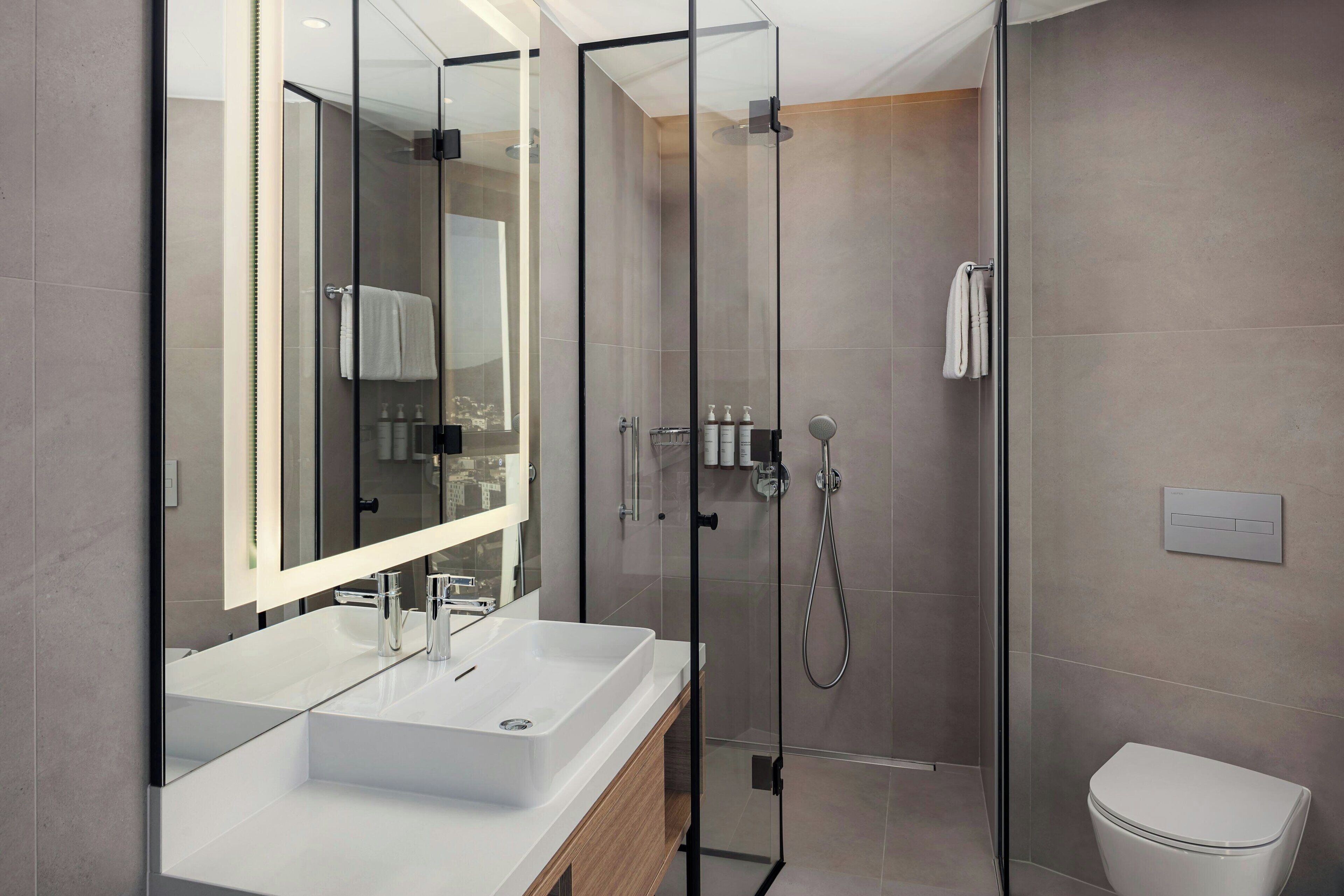 Un baño moderno con ducha de vidrio, lavamanos blanco y retrete.