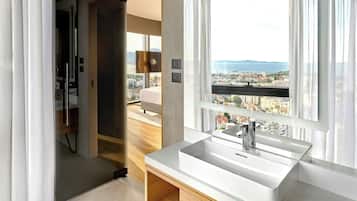 Ein modernes Badezimmer mit großem Fenster, einem weißen Waschbecken und Blick auf eine Stadtansicht.