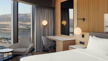 Une chambre d’hôtel moderne dotée d’un grand lit, d’un bureau, d’une chaise et offrant une vue sur un paysage montagneux grâce à de grandes fenêtres.